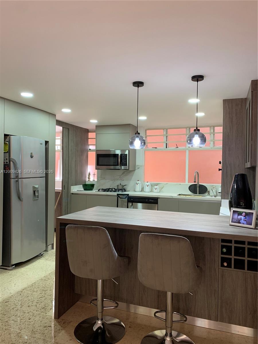 A modern kitchen features a breakfast bar, stainless steel appliances, and wood-toned cabinetry — Carrera 44 17 SUR 70 # 302, AN 050018, AN
