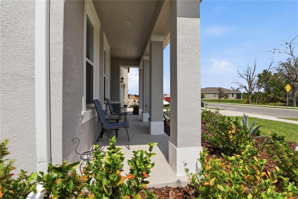 A covered front porch with gray stucco columns and two chairs overlooks a suburban street — 11957 KINGSLEY TRAIL, PARRISH, FL