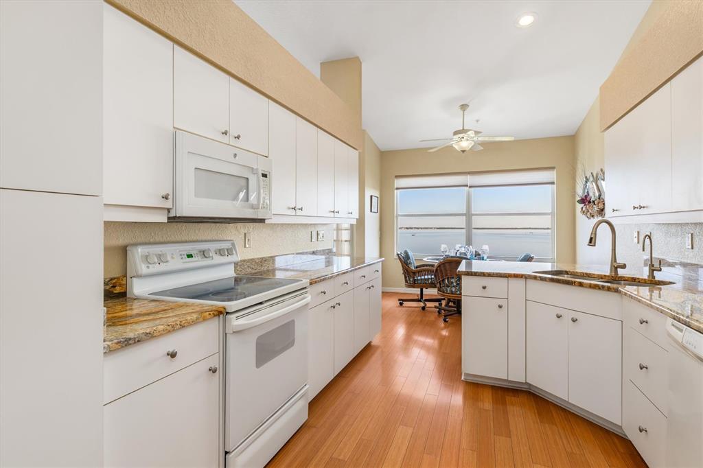 A kitchen with white cabinets, granite countertops, and a dining area overlooking the water — 200 HARBOR WALK DRIVE UNIT 354, PUNTA GORDA, FL