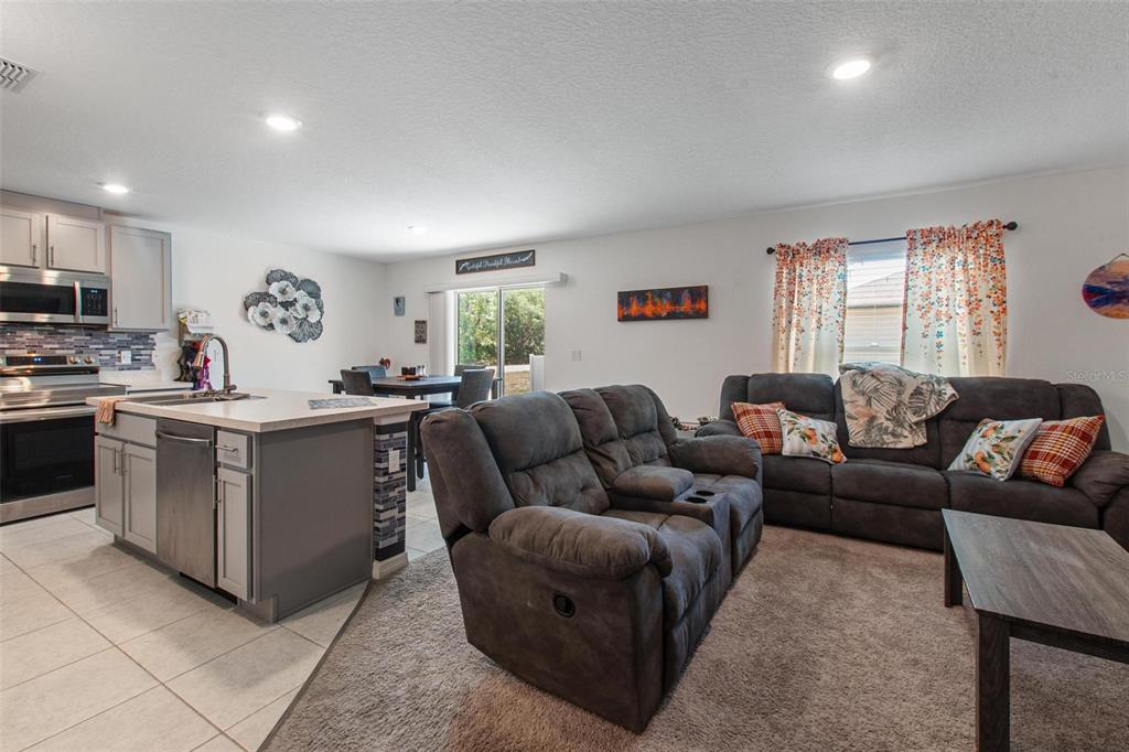 An open-concept kitchen with a center island flows into a living area with gray furniture — 500 RIO GRANDE DRIVE, KISSIMMEE, FL