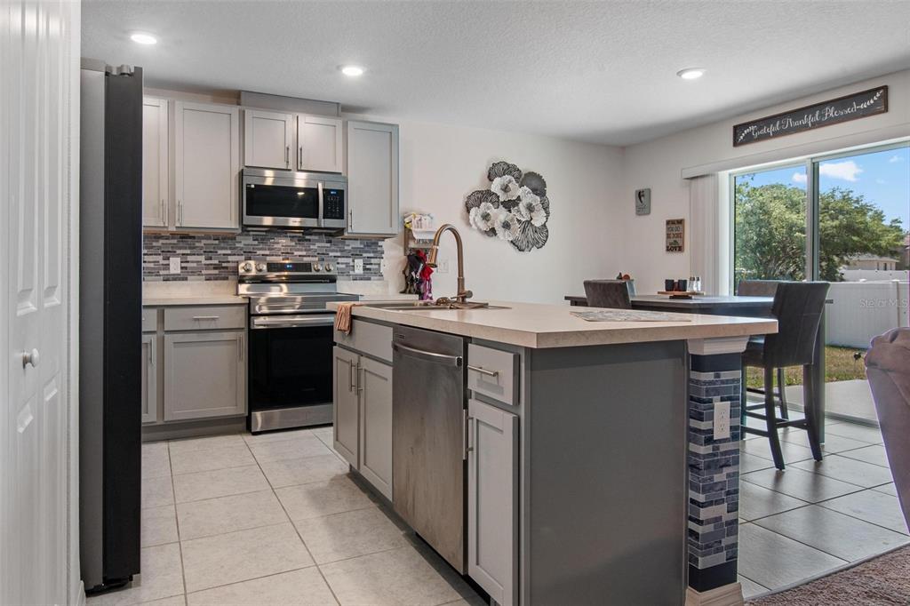 A kitchen features gray cabinetry, a central island with a dishwasher, and stainless steel appliances — 500 RIO GRANDE DRIVE, KISSIMMEE, FL