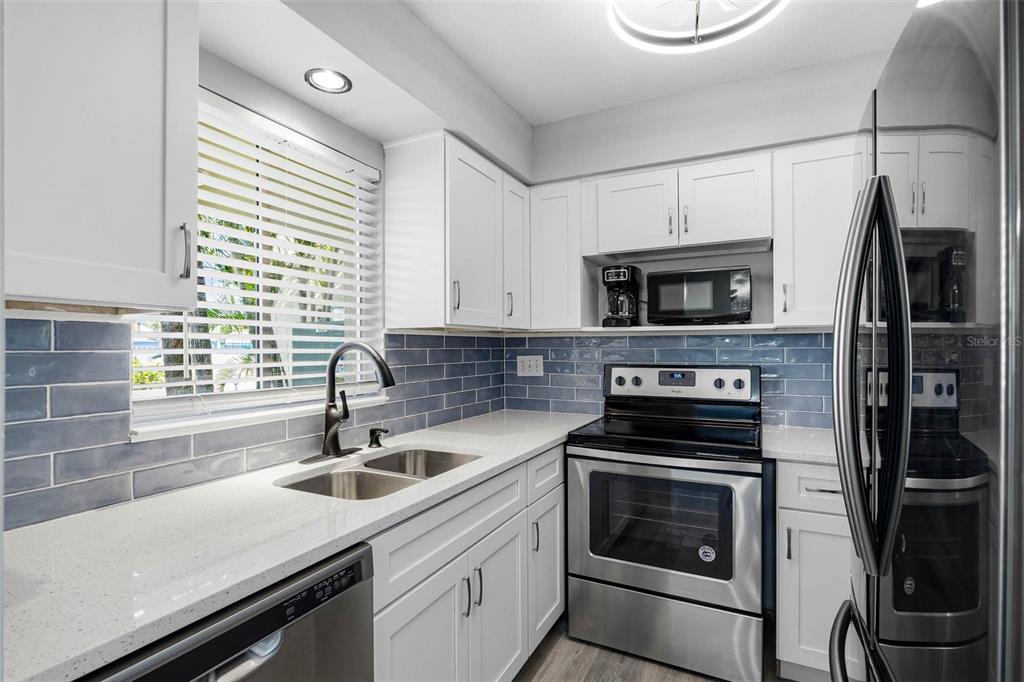 A kitchen with white cabinets, stainless steel appliances, quartz countertops, and blue subway tile backsplash — 2900 45TH STREET S UNIT 7, GULFPORT, FL