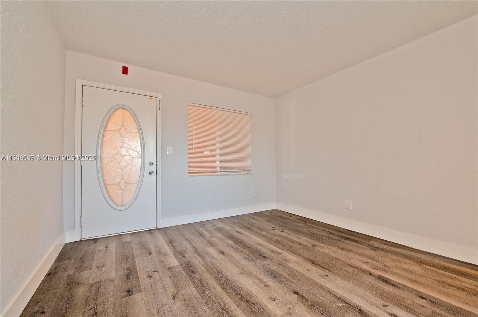 An empty room features light gray walls, wood-look flooring, a white front door, and a window — 2330 NW 11th St # 47, Miami FL 33125, MIAMI, FL