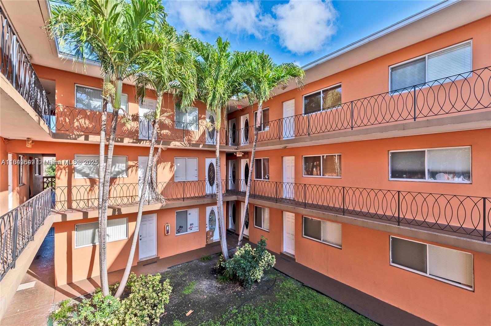 An exterior view of a three-story orange apartment building with open walkways and palm trees — 2330 NW 11th St # 47, Miami FL 33125, MIAMI, FL
