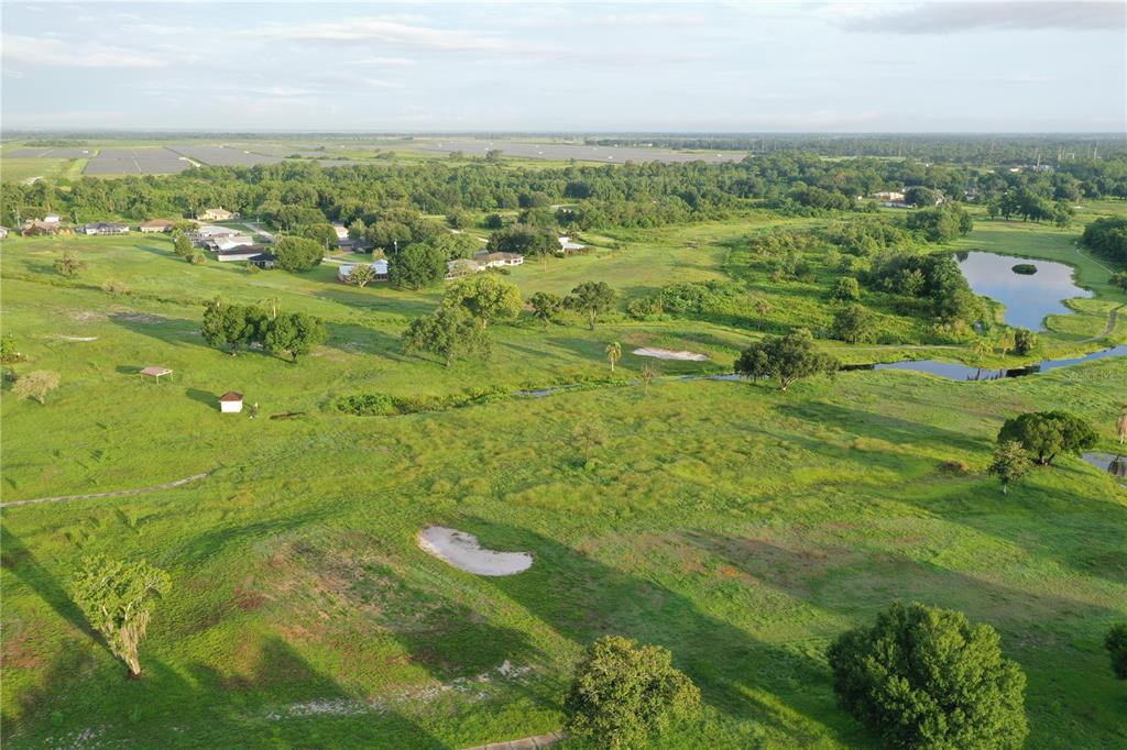 An aerial view of a grassy landscape with scattered trees, sand bunkers, and a small pond — 119 LINCOLN ROAD NW, LAKE PLACID, FL