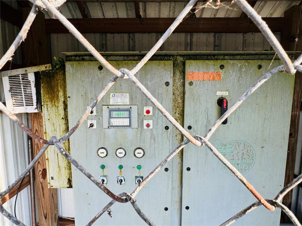 A weathered industrial control panel sits behind a chain-link fence in an outdoor structure — 119 LINCOLN ROAD NW, LAKE PLACID, FL