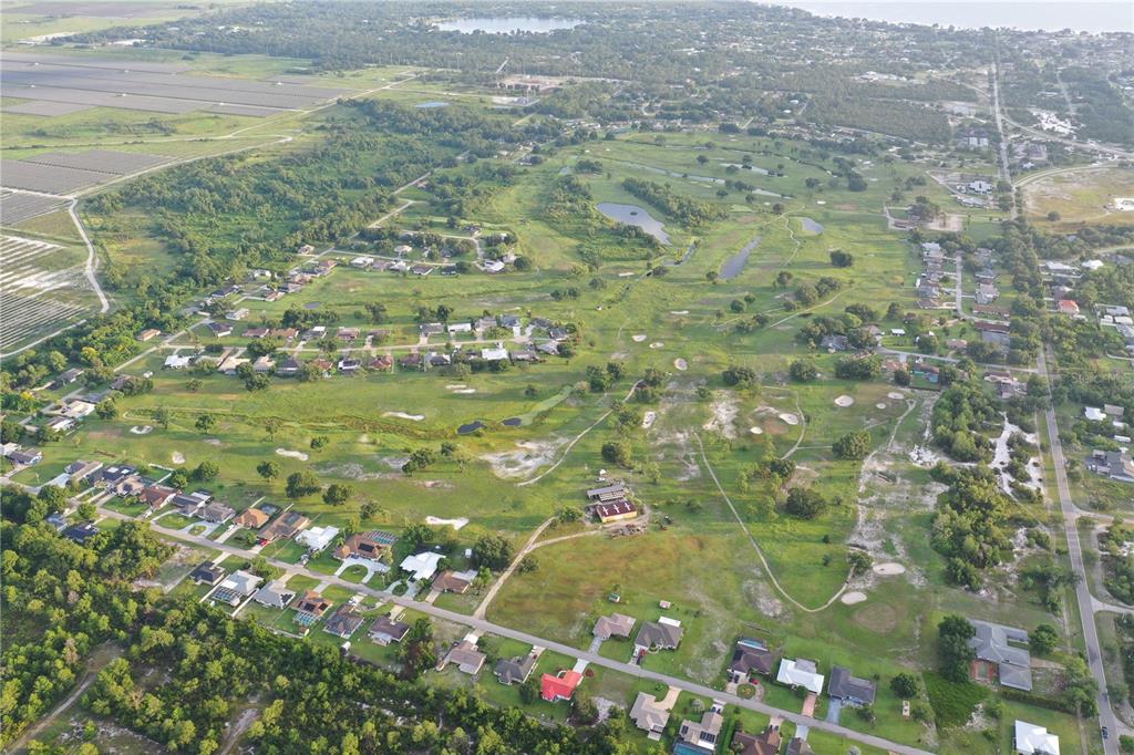 An aerial view shows a residential neighborhood surrounding a large, grassy golf course with ponds — 119 LINCOLN ROAD NW, LAKE PLACID, FL