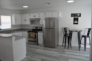 A kitchen features white cabinets, stainless steel appliances, a small dining table, and gray flooring — 6516 E 25TH AVENUE, TAMPA, FL