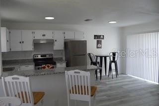 A kitchen features white cabinets, stainless steel appliances, a breakfast bar, and light wood flooring — 6516 E 25TH AVENUE, TAMPA, FL