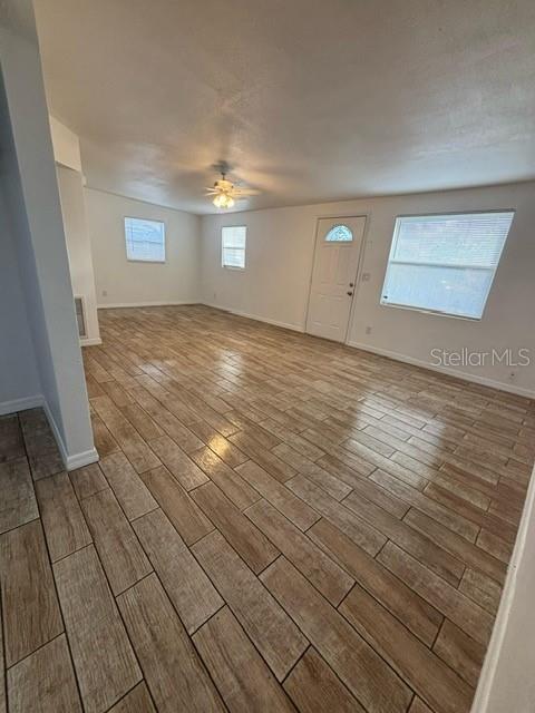 An empty room features wood-look tile flooring, a ceiling fan, and a white front door — 4554 NIMMER DRIVE, NEW PORT RICHEY, FL