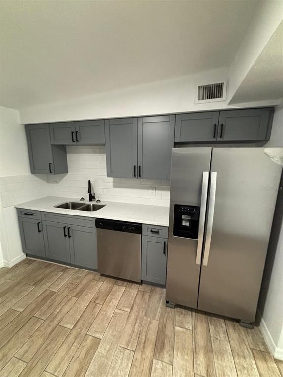 A kitchen features gray cabinets, stainless steel appliances, white countertops, and wood-look tile flooring — 4554 NIMMER DRIVE, NEW PORT RICHEY, FL
