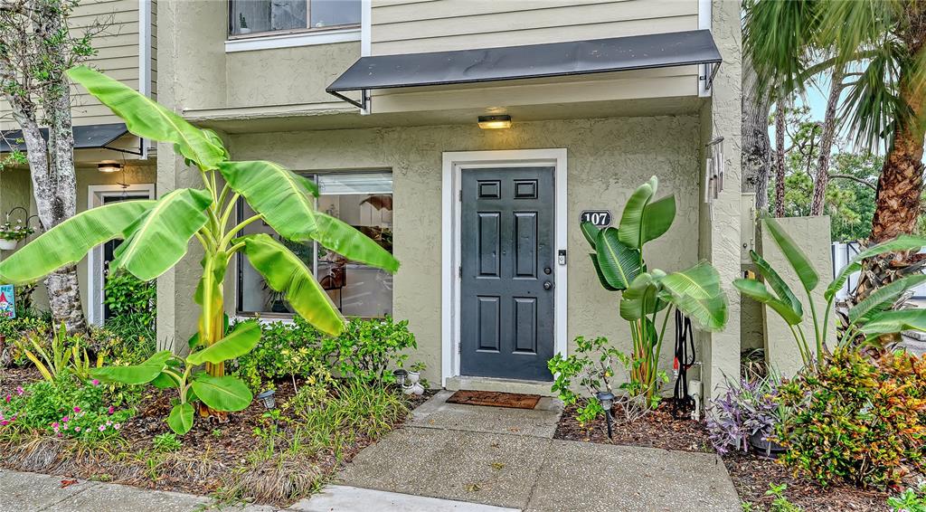 The exterior of a residential unit features a gray front door labeled 107 and landscaping — 4906 25TH STREET W UNIT 107, BRADENTON, FL