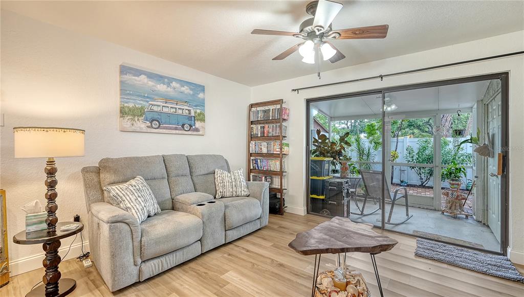 A living room features a gray reclining sofa, wood-look flooring, and a sliding glass door — 4906 25TH STREET W UNIT 107, BRADENTON, FL