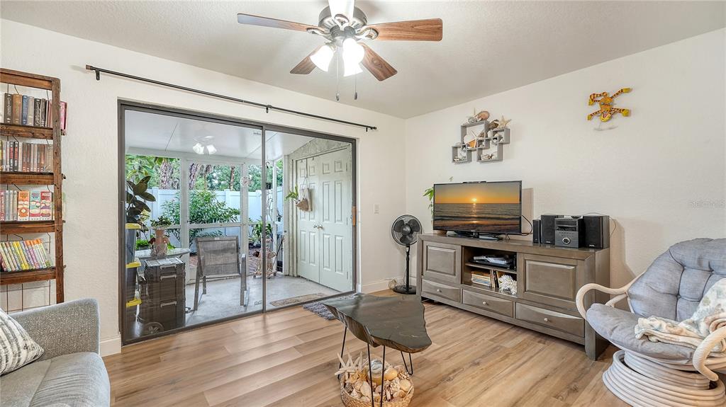 A living room with wood-look flooring, a ceiling fan, a media console, and sliding glass doors — 4906 25TH STREET W UNIT 107, BRADENTON, FL