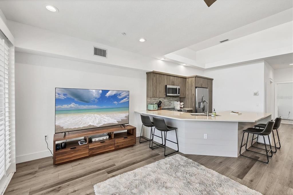 A modern kitchen with a breakfast bar and living area featuring a large television — 8234 HARBORSIDE CIRCLE, ENGLEWOOD, FL