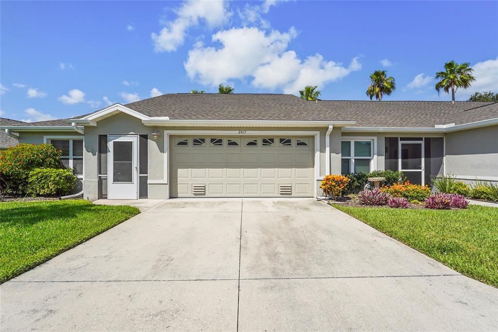 A single-story house exterior features a beige garage, a white front door, and landscaped lawn — 2417 FAIRWAY OAKS DRIVE UNIT 22, PALMETTO, FL