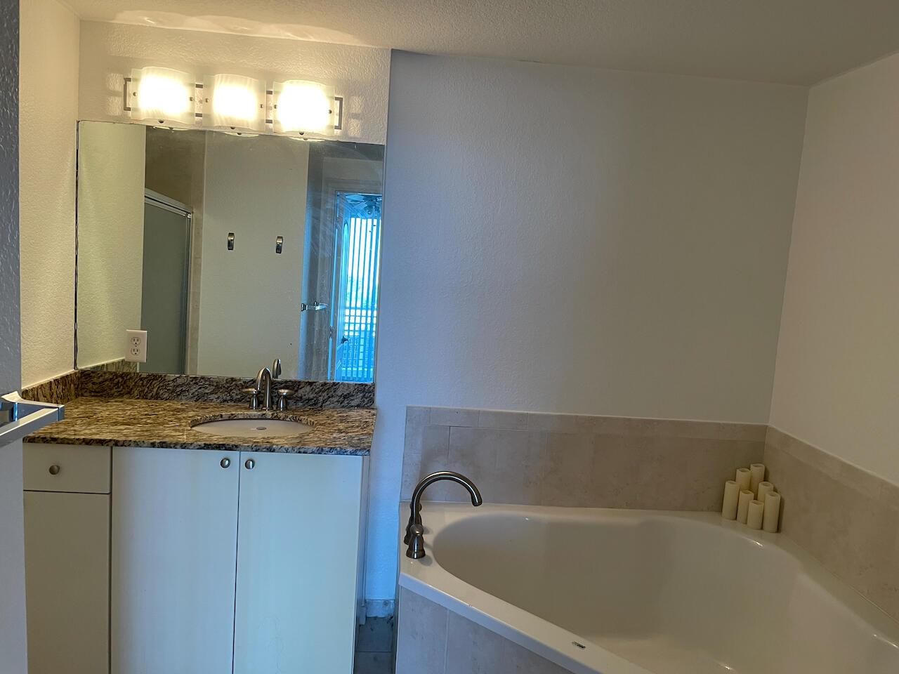 A bathroom features a granite vanity, a white cabinet, a mirror, and a corner bathtub — 1830 Radius Drive # 307, Hollywood FL 33020, HOLLYWOOD, FL