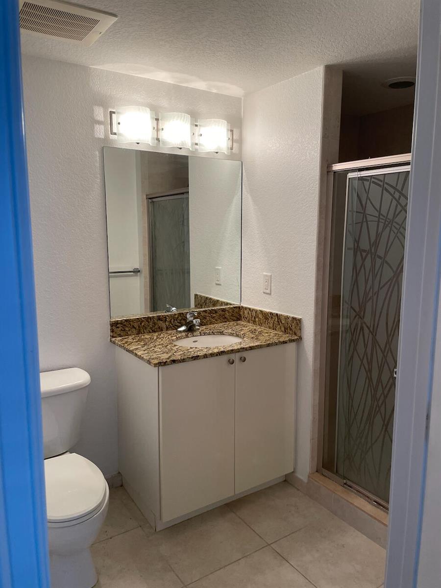A bathroom features a white vanity with a granite countertop, a mirror, and a shower — 1830 Radius Drive # 307, Hollywood FL 33020, HOLLYWOOD, FL