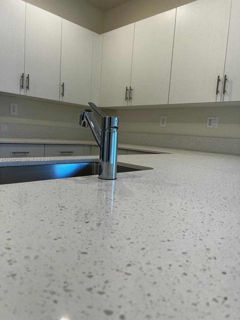 A modern kitchen features white cabinets, a speckled quartz countertop, and a chrome faucet — 11444 W 33rd Ct # 0, Hialeah FL 33018, HIALEAH, FL