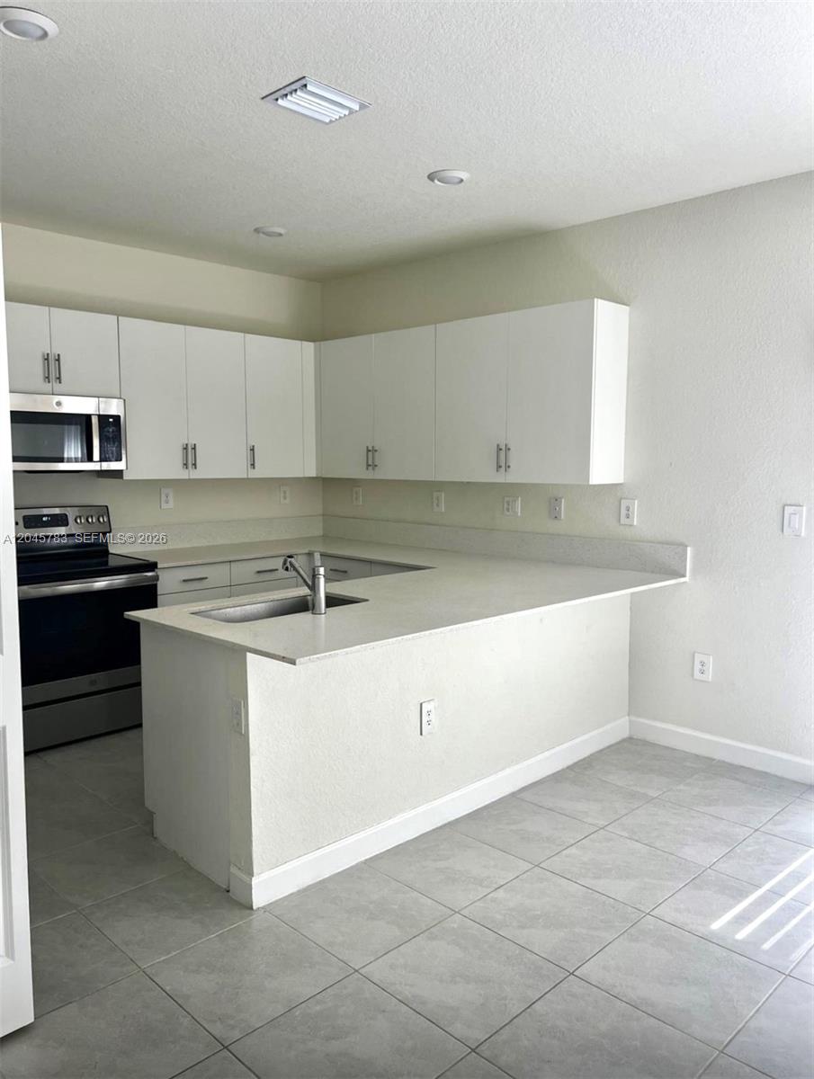 A kitchen features white cabinets, stainless steel appliances, and a peninsula with a sink — 11444 W 33rd Ct # 0, Hialeah FL 33018, HIALEAH, FL