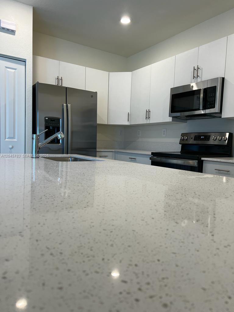 A kitchen features white cabinets, stainless steel appliances, and a speckled quartz countertop island — 11444 W 33rd Ct # 0, Hialeah FL 33018, HIALEAH, FL