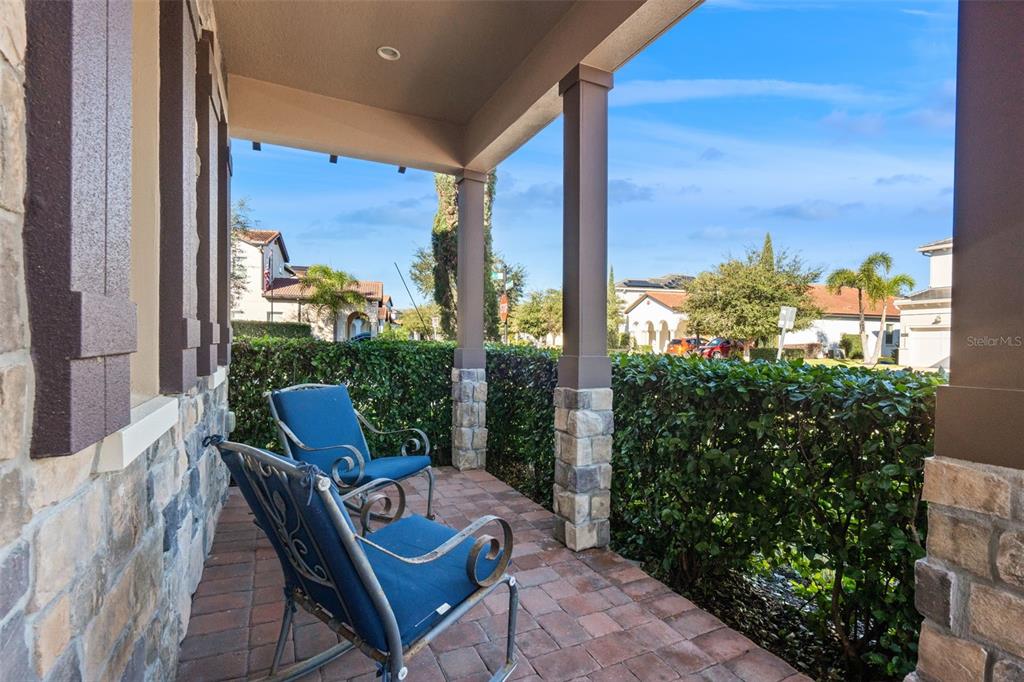 A covered front porch features stone-based columns, brick pavers, and two blue rocking chairs — 15672 SHOREBIRD LANE, WINTER GARDEN, FL