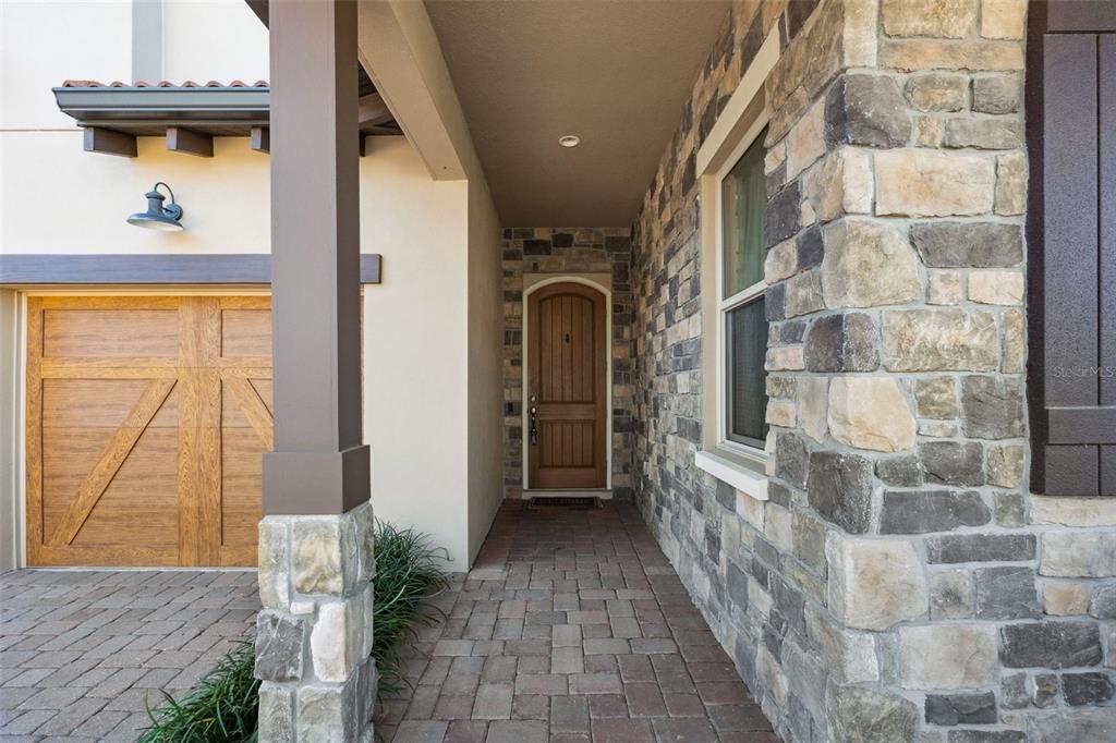 A stone-clad entryway features a wooden front door, a brick walkway, and a garage — 15672 SHOREBIRD LANE, WINTER GARDEN, FL