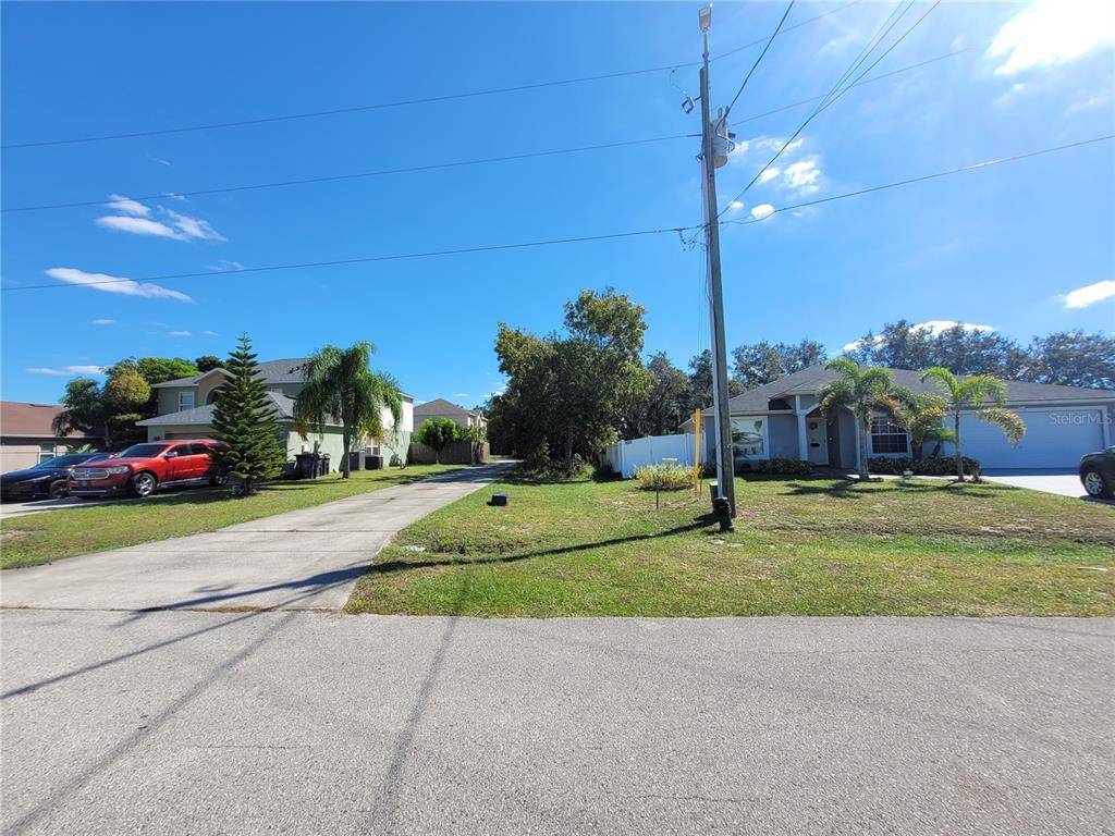 A street view shows two houses with driveways, a utility pole, and trees under a blue sky — 1929 MANATEE DRIVE, POINCIANA, FL