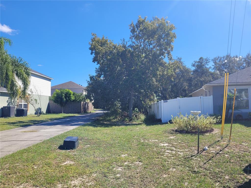 A grassy yard features a paved driveway, a large tree, and a white privacy fence — 1929 MANATEE DRIVE, POINCIANA, FL