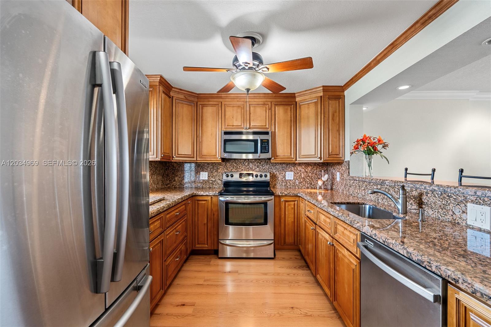 A kitchen features wood cabinets, granite countertops, stainless steel appliances, and a ceiling fan — 325 SE 11th Ter # 308, Dania Beach FL 33004, DANIA BEACH, FL