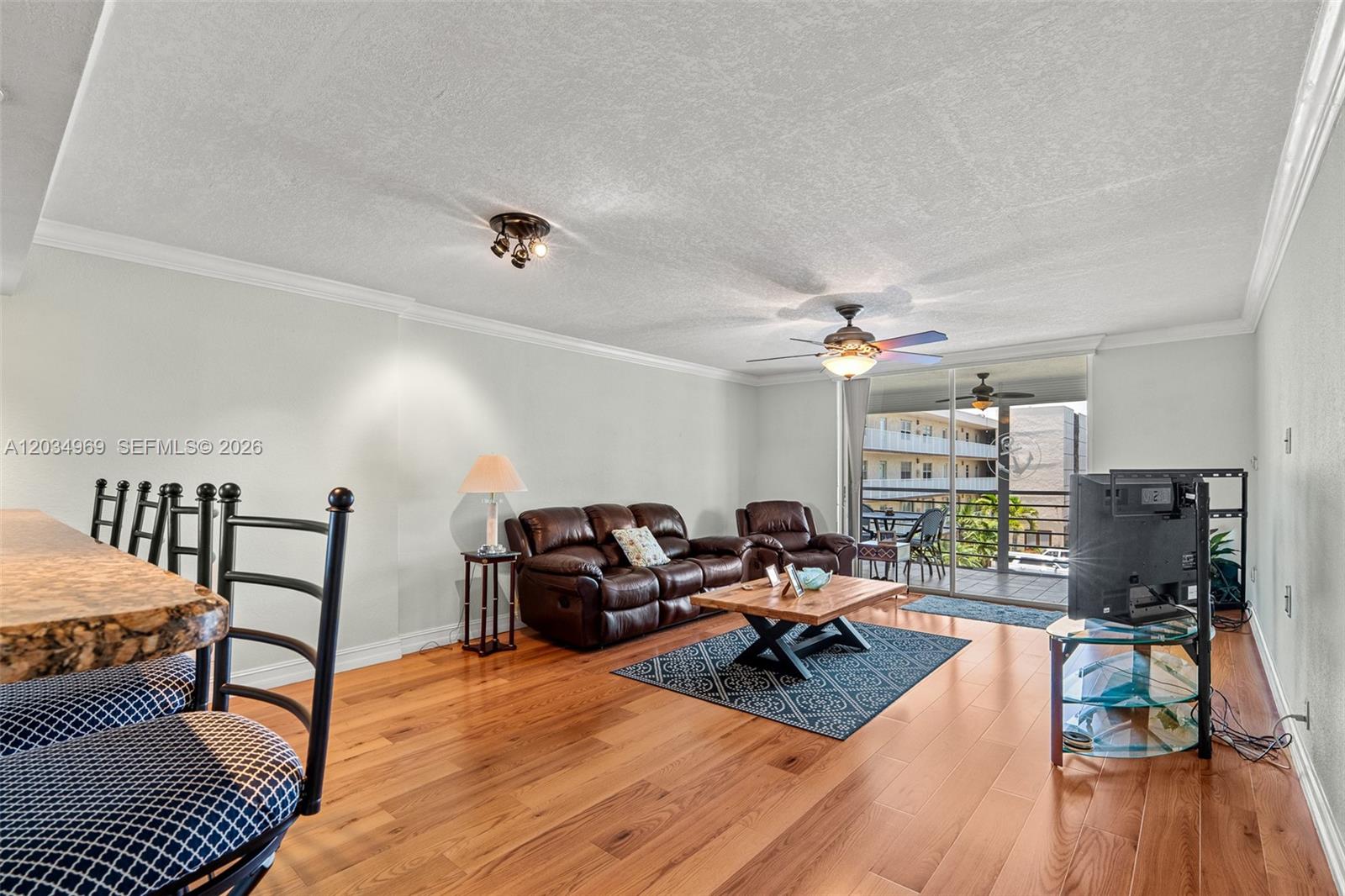 A living room features hardwood floors, a brown leather sofa, and a balcony with seating — 325 SE 11th Ter # 308, Dania Beach FL 33004, DANIA BEACH, FL