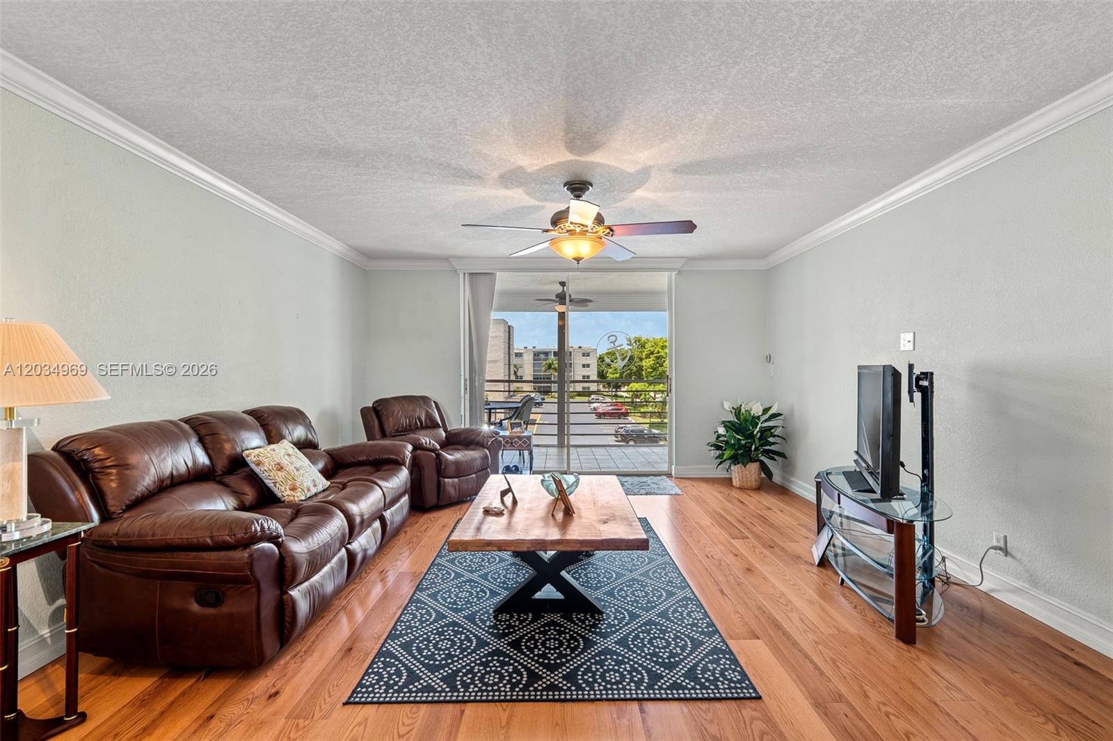 A living room features a brown leather sofa, wood coffee table, and sliding glass balcony doors — 325 SE 11th Ter # 308, Dania Beach FL 33004, DANIA BEACH, FL