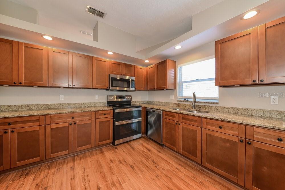 A kitchen features wood cabinets, granite countertops, stainless steel appliances, and wood-look flooring — 12914 ASTORWOOD PLACE, RIVERVIEW, FL