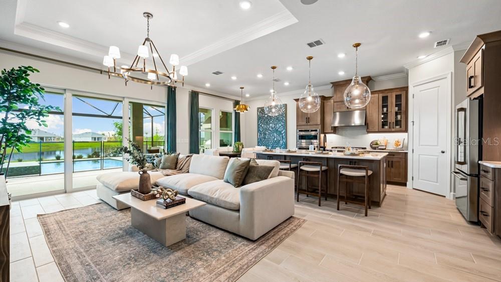 An open-concept living room and kitchen feature a large sectional, island seating, and pool views — 26120 ASPARANO AVENUE, ENGLEWOOD, FL