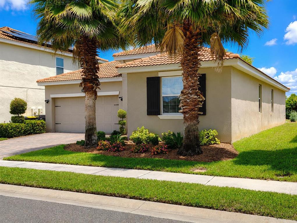 A tan single-story house with a two-car garage, tile roof, and two palm trees — 1047 OAK BLUFF DRIVE, DAVENPORT, FL