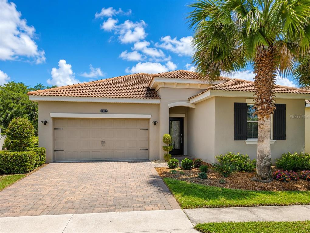A single-story house with a tan stucco exterior, a tile roof, and a paved driveway — 1047 OAK BLUFF DRIVE, DAVENPORT, FL