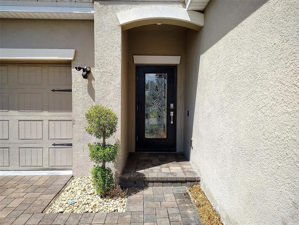 The exterior view shows a tan stucco home with a dark front door and pavers — 1047 OAK BLUFF DRIVE, DAVENPORT, FL