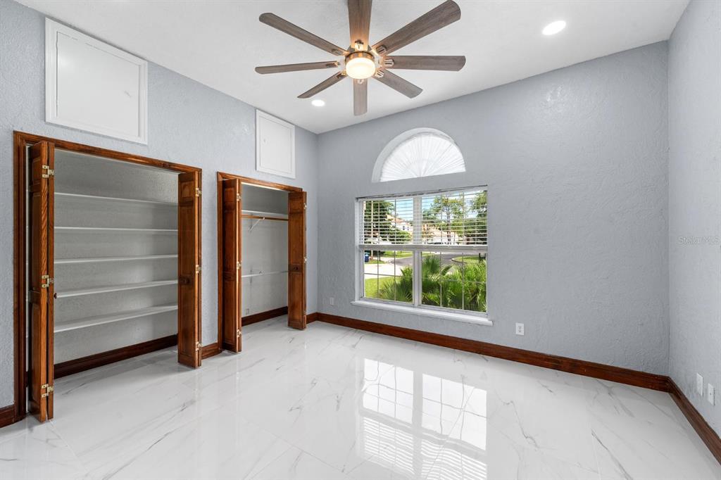 A bedroom with white marble-look tile floors, two wooden closets, and a large arched window — 2985 LA CONCHA DRIVE, CLEARWATER, FL