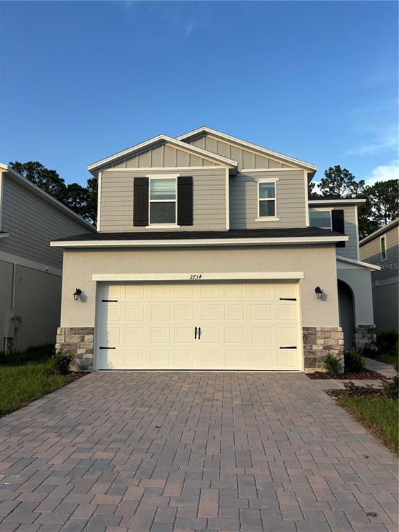 A two-story house features a gray exterior, a stone-accented base, and a paved driveway — 2734 RAINDROP RUN ST, CLERMONT, FL