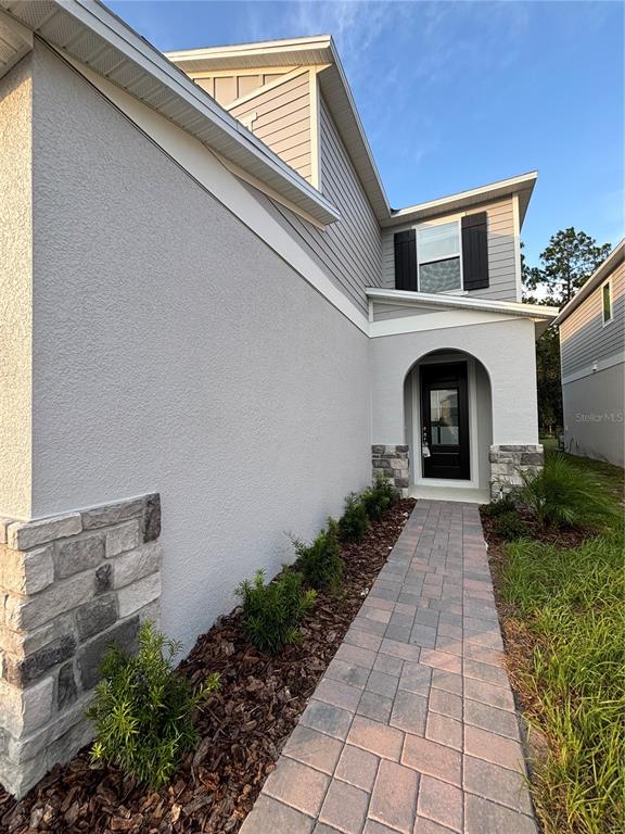 A paved walkway leads to the front entrance of a two-story house with stone accents — 2734 RAINDROP RUN ST, CLERMONT, FL