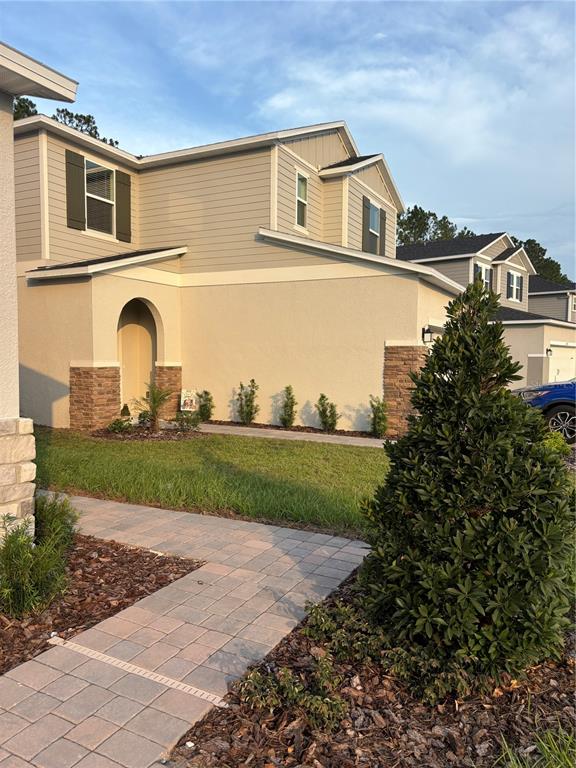 A two-story house with beige siding, stucco walls, and stone accents features a paved walkway — 2734 RAINDROP RUN ST, CLERMONT, FL