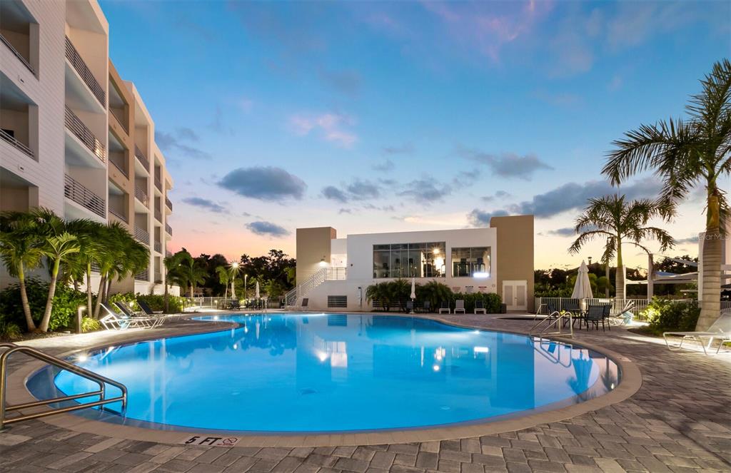 A swimming pool sits in front of a modern multi-story building at sunset — 1703 N TAMIAMI TRAIL UNIT 306, SARASOTA, FL
