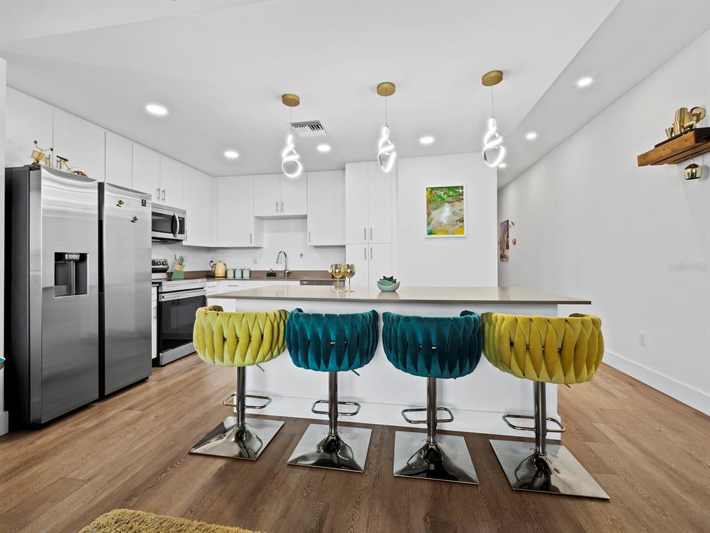 A modern kitchen features white cabinetry, stainless steel appliances, and four colorful velvet bar stools — 1703 N TAMIAMI TRAIL UNIT 306, SARASOTA, FL