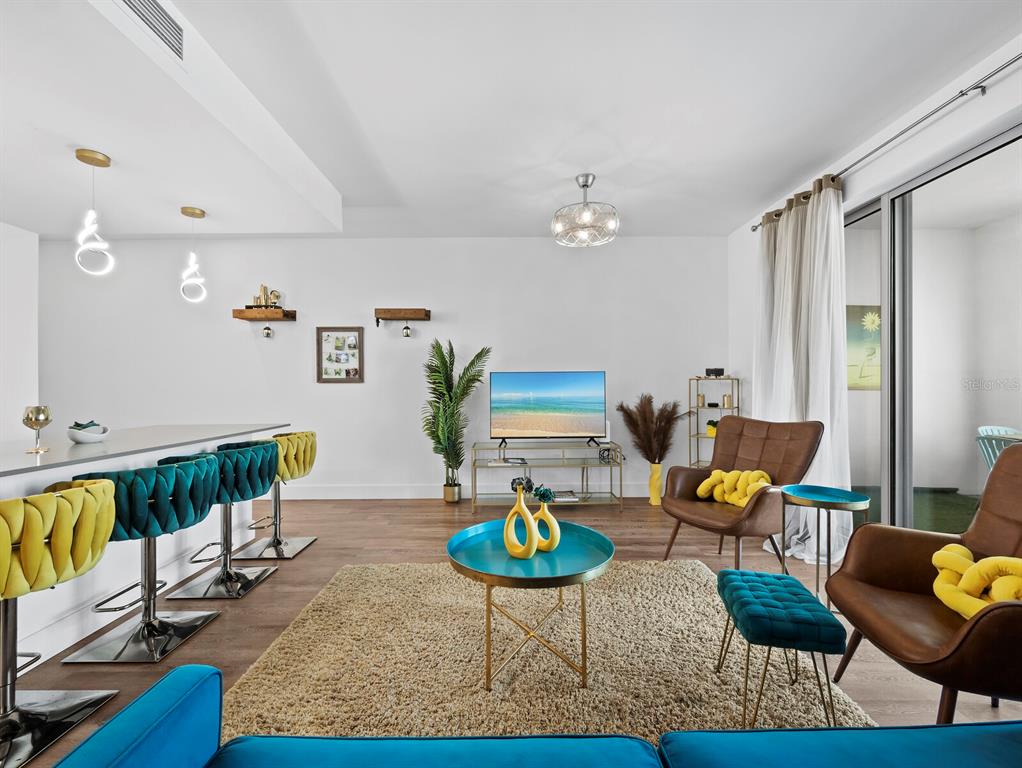 A modern living room features a breakfast bar, teal and yellow furniture, and a television — 1703 N TAMIAMI TRAIL UNIT 306, SARASOTA, FL