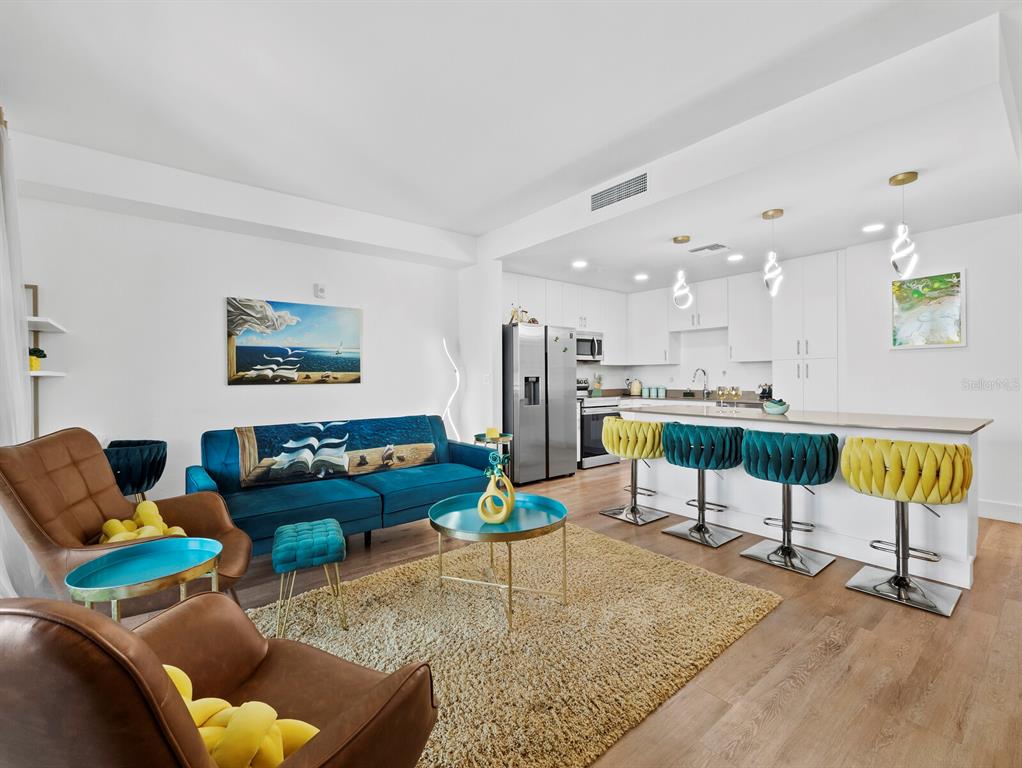 An open-concept living room and kitchen featuring a blue sofa, brown armchairs, and a breakfast bar — 1703 N TAMIAMI TRAIL UNIT 306, SARASOTA, FL