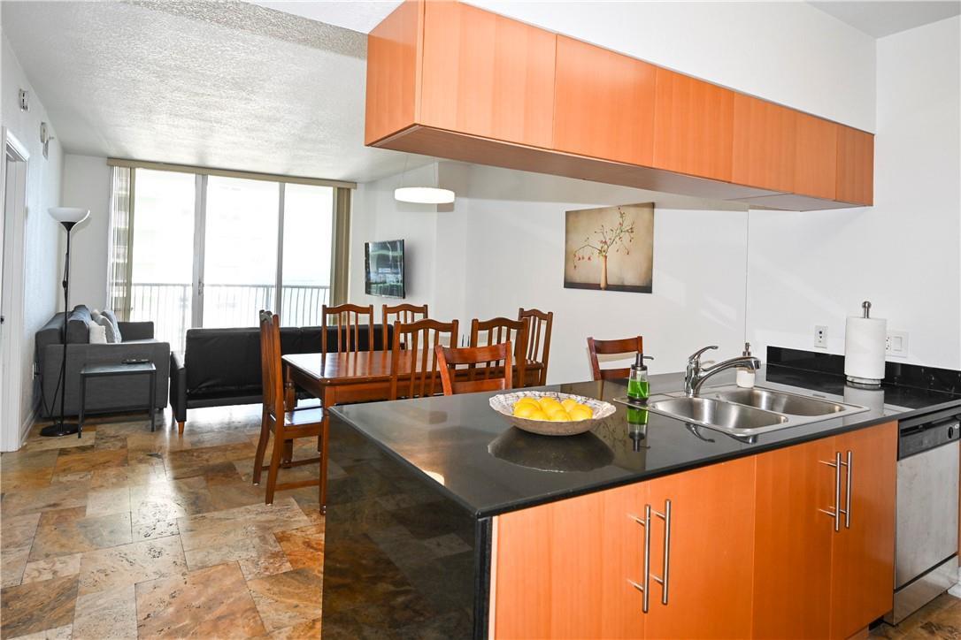 A kitchen with orange cabinets and black countertops overlooks a dining area and living room — 1750 N Bayshore Drive # 2403, Miami FL 33132, MIAMI, FL
