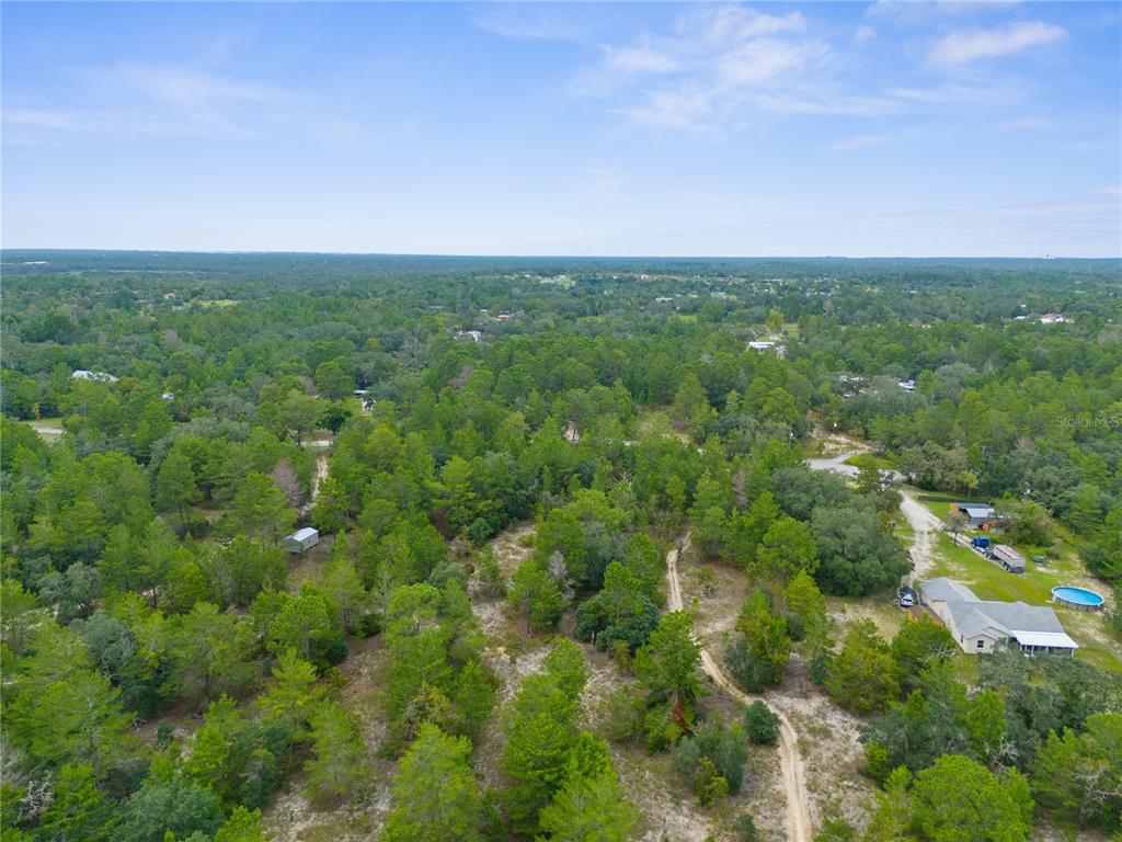 An aerial view shows a wooded lot with a dirt path and nearby residential houses — MADISON STREET, BROOKSVILLE, FL