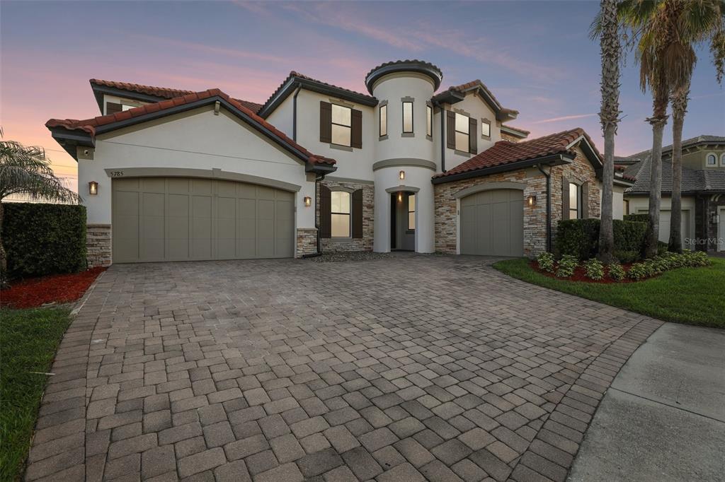 A two-story house with a paver driveway, stone accents, and a three-car garage at dusk — 5785 SAYBROOK CIRCLE, SANFORD, FL