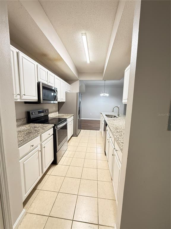 A galley kitchen features white cabinets, granite countertops, stainless steel appliances, and tile flooring — 12017 VILLANOVA DRIVE UNIT 109, ORLANDO, FL