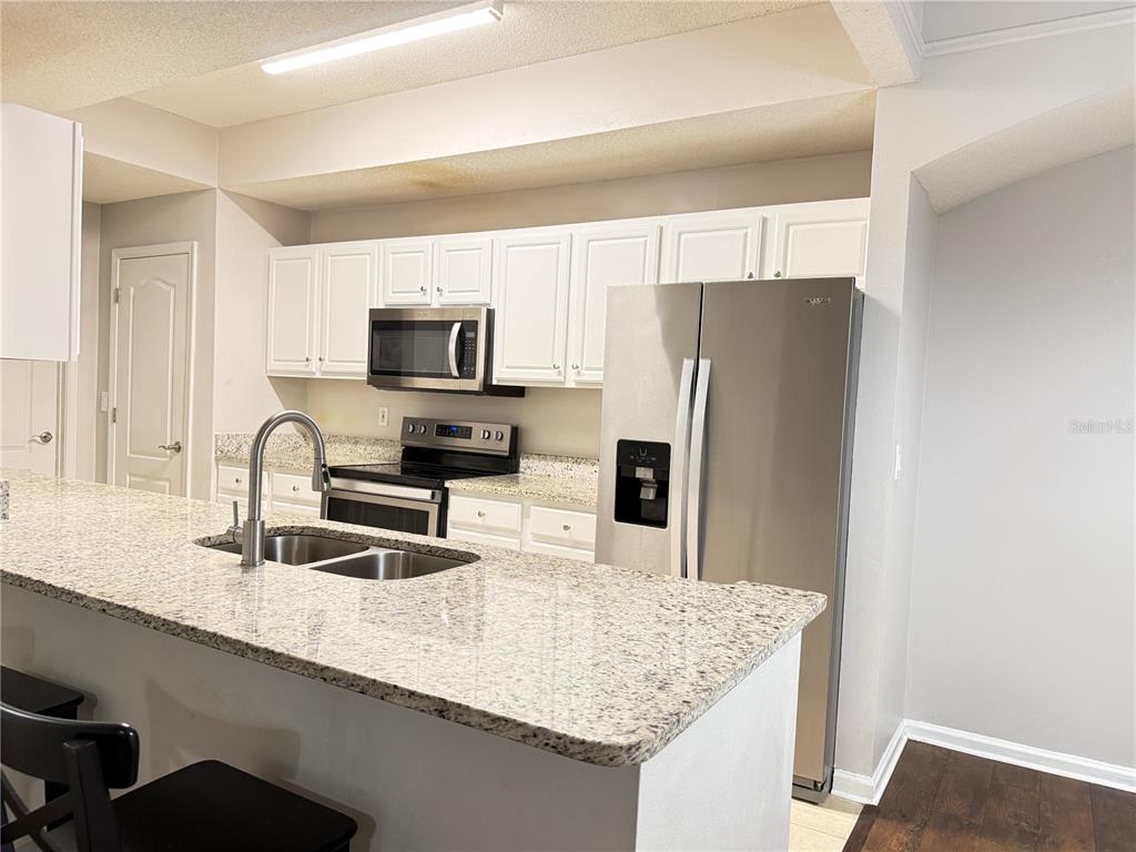 A kitchen features white cabinets, granite countertops, and stainless steel appliances — 12017 VILLANOVA DRIVE UNIT 109, ORLANDO, FL